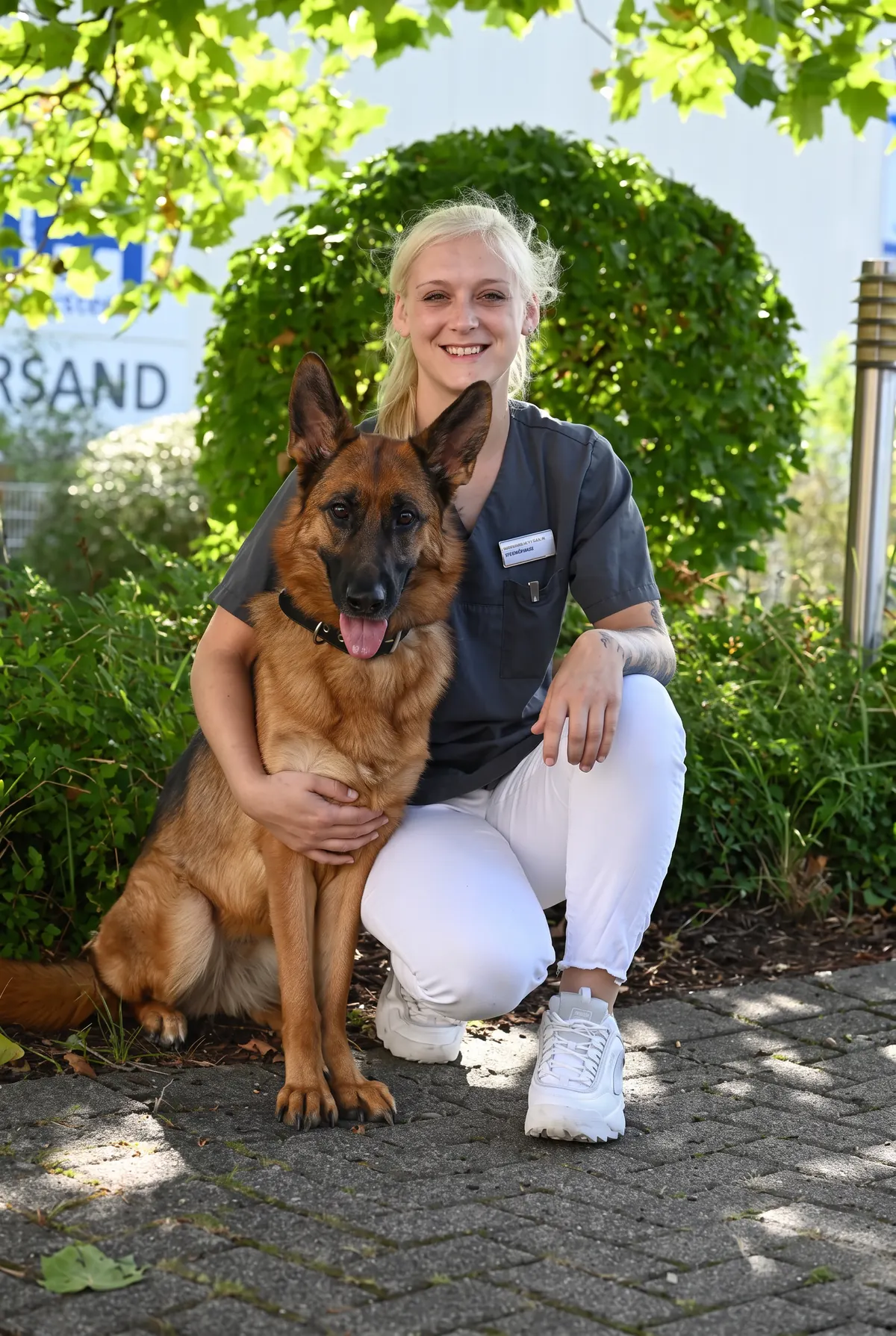 Mitarbeiterin mit Schäferhund vor der Praxis